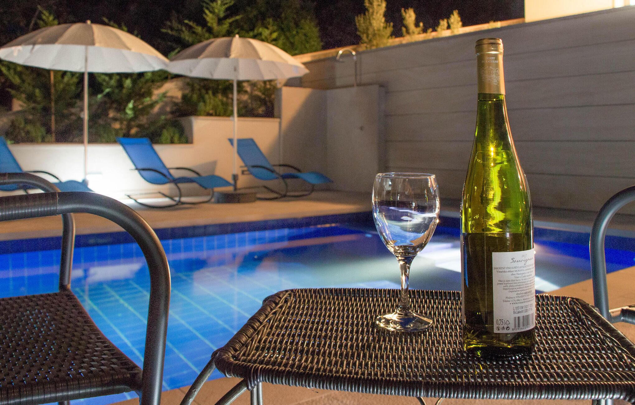 A poolside setting with a bottle of wine and a glass on a chair.