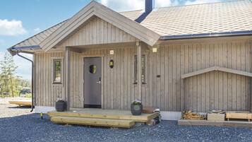 A wooden cabin with a front porch, a door with a circular window, and two planters with flowers.