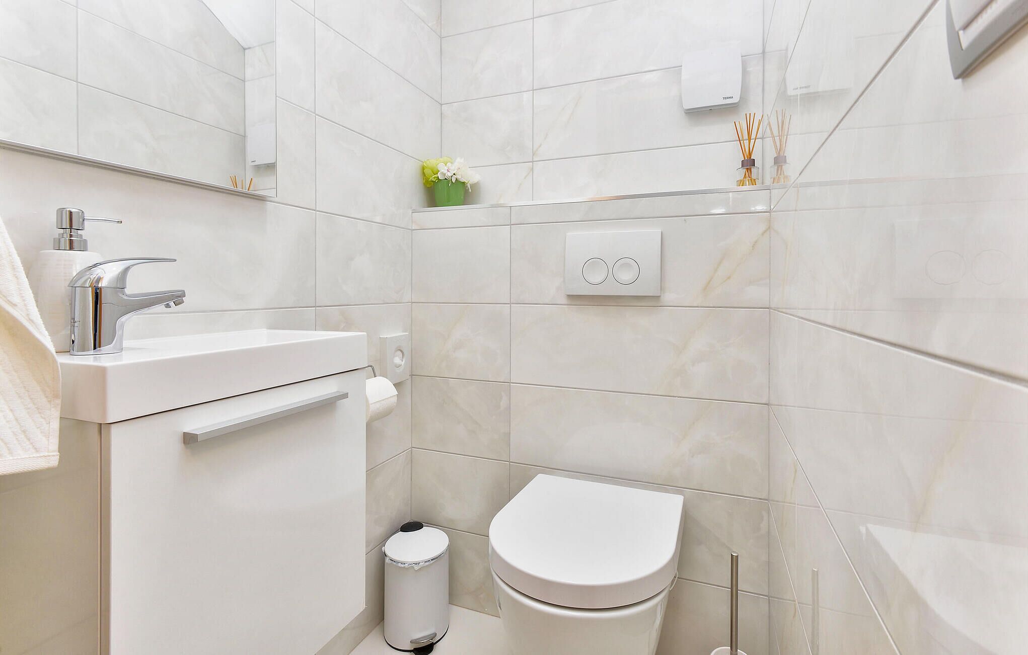 A modern bathroom with a white sink, toilet, and shower area.