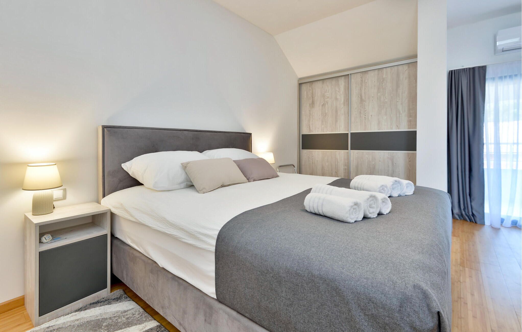 Een moderne hotelkamer met een groot bed, een nachtkastje met een lamp, een kledingkast en uitzicht op het omliggende landschap.