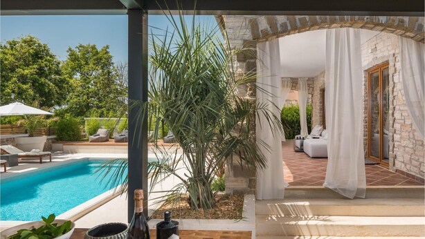 A pool area with lounge chairs, a bottle of wine, and a potted plant. - Luxurious home in Cabrunici with sauna (Cabrunici)