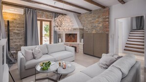 A modern living room with a stone fireplace, a grey sofa, and a round coffee table with candles. - Luxurious home in Cabrunici with sauna (Cabrunici)