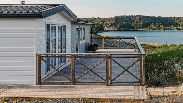 Un chalet au bord du lac, doté d’une terrasse en bois et offrant une vue sur le lac.