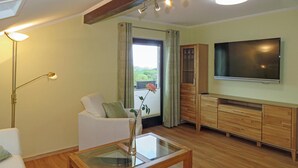 Un salon moderne avec un canapé, une table basse en verre, un téléviseur, des meubles en bois et une grande fenêtre avec des rideaux.