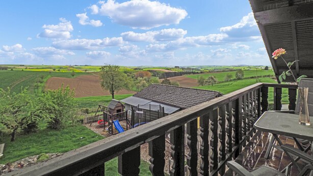 Un balcon donnant sur un paysage rural, avec des champs et une aire de jeux.