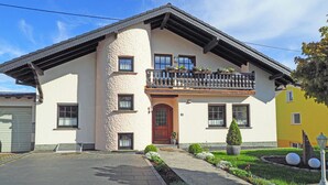 Une maison à deux étages avec un balcon, une porte d’entrée et un petit jardin.
