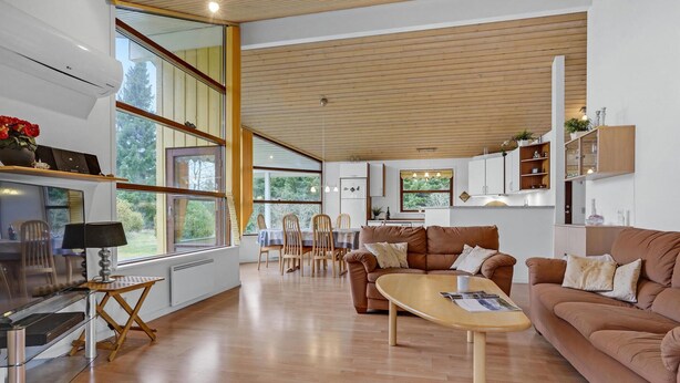 A spacious living room with a wooden floor, a brown sofa, a coffee table, and a dining area with chairs and a table. - Awesome home in Hals with kitchen (Hals)