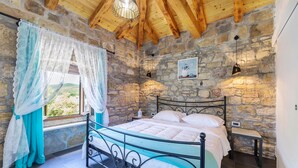 A bedroom with a stone wall, a bed with a metal frame, a nightstand, a window with curtains, and a hanging light fixture. - Gorgeous home in Zarecje with WiFi (Zarecje)