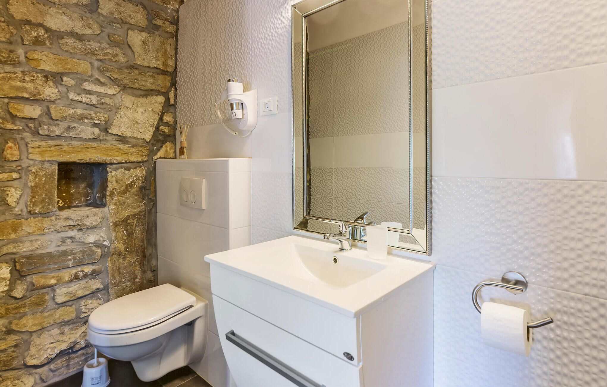 A bathroom with a stone wall, a white sink, a mirror, and a toilet.