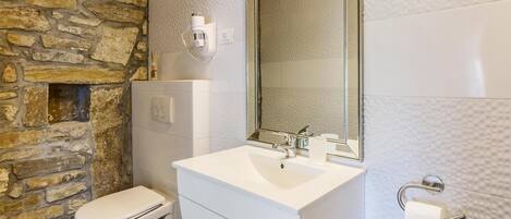 A bathroom with a stone wall, a white sink, a mirror, and a toilet.