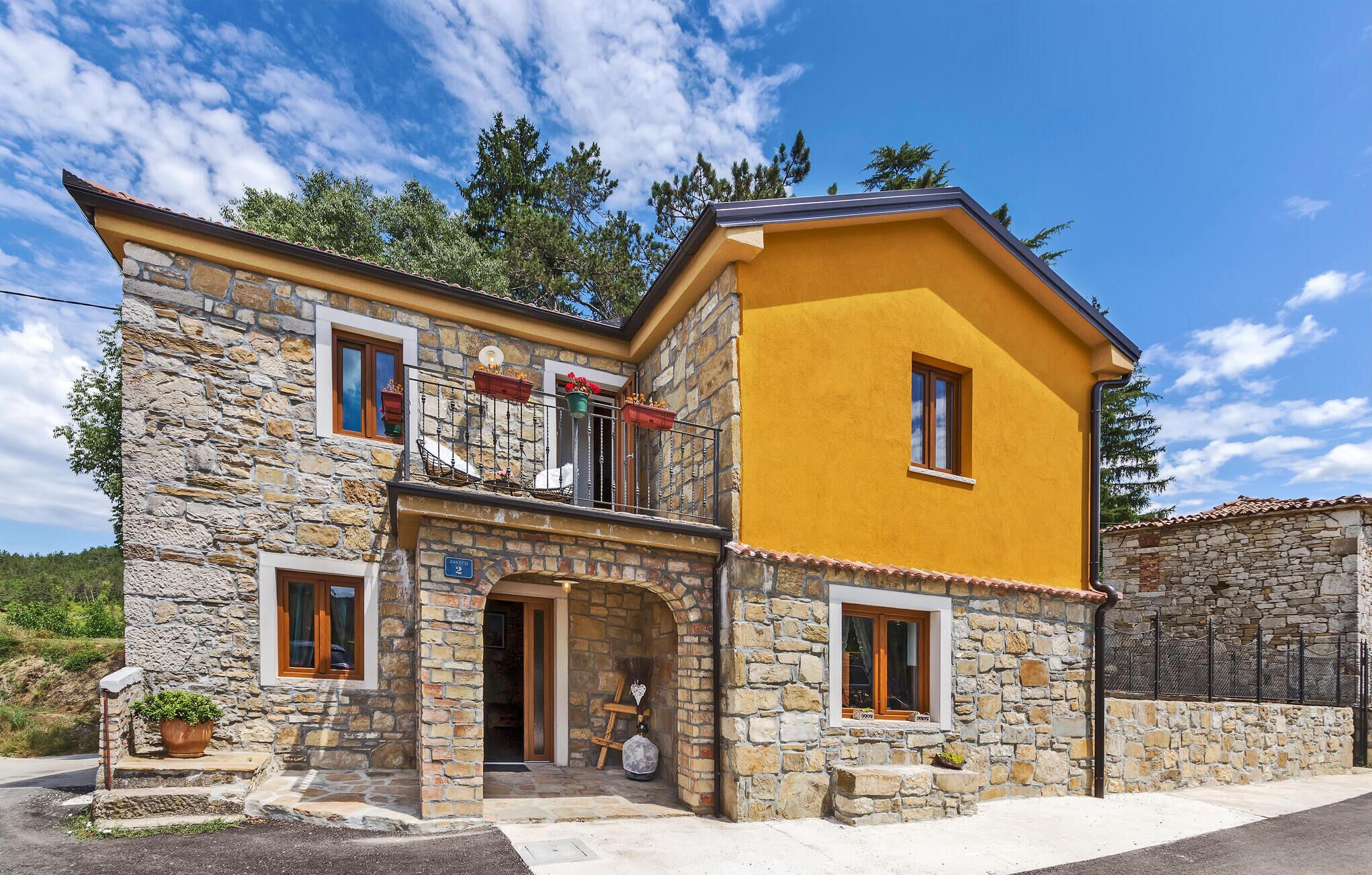 Une maison en pierre à deux étages, avec une façade jaune, des marches en pierre et un balcon orné de jardinières.