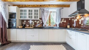 A kitchen with white cabinets, a black stove, and a window with lace curtains. - Gorgeous home in Zarecje with WiFi (Zarecje)