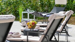 A poolside lounge area with reclining chairs, a wicker table with a fruit bowl, and a lounge chair with a towel. - Luxurious home in Rukljevina with sauna (Rukljevina)