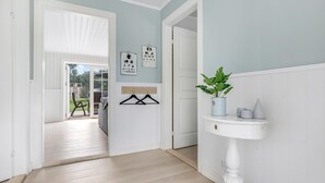A hallway with a wooden floor, a white door, and a wall-mounted shelf with a plant and decorative items.