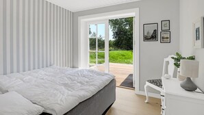 A bedroom with a bed, a chair, a desk, and a view of the outdoors through a glass door.