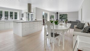 A spacious kitchen with white cabinetry, a central island, and a dining area with white chairs and a table.