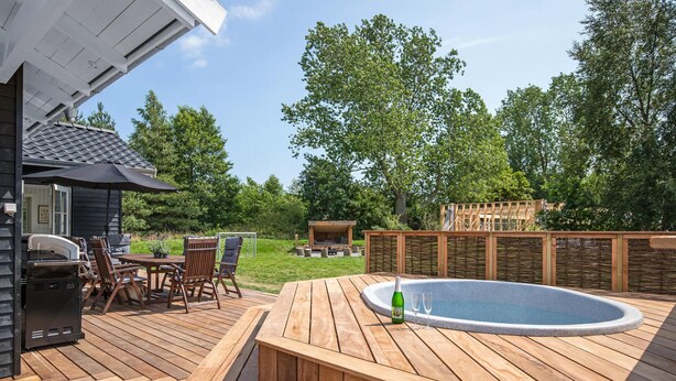 A wooden deck with a hot tub, outdoor seating, and a barbecue area.