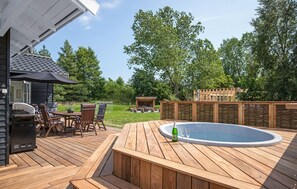 A wooden deck with a hot tub, outdoor seating, and a barbecue area.
