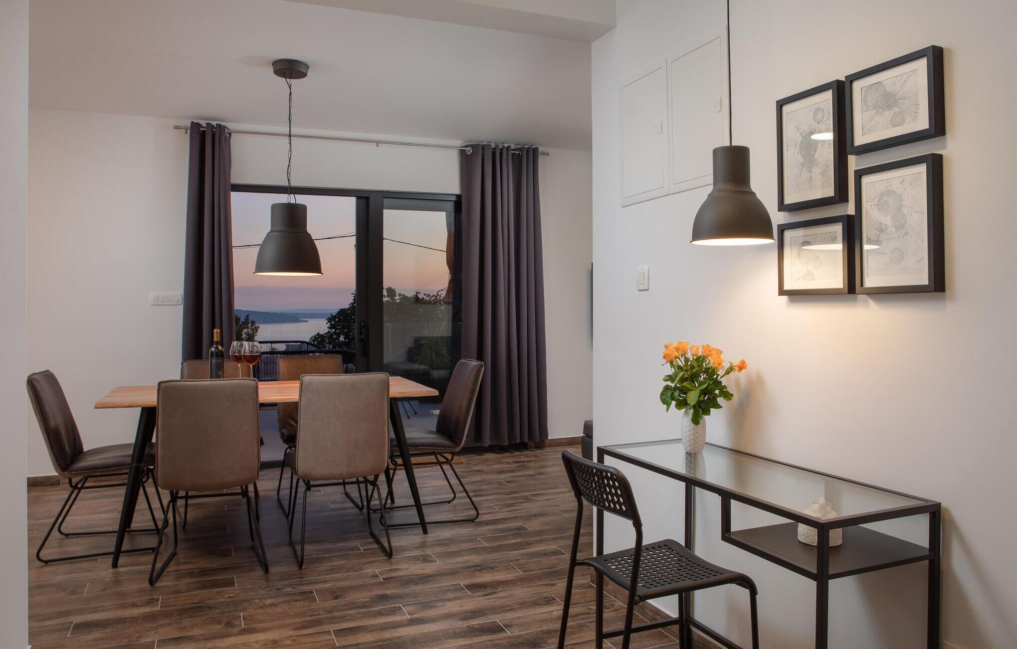 A modern dining area with a wooden table and chairs, a glass coffee table, and a view of the outdoors.