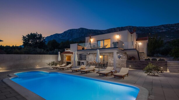 Ein modernes, zweistöckiges Haus mit Swimmingpool, Außenbereich zum Sitzen und einer Bergkulisse.