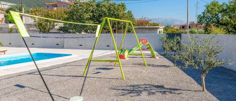 A pool area with a swing set and a small tree.