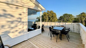 Une terrasse extérieure avec une table et des chaises, donnant sur une étendue d’eau et des arbres.