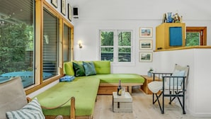 Un salon chaleureux avec un canapé d’angle vert, une table basse en bois et une petite table d’appoint. Des tableaux encadrés ornent le mur, et un buffet bleu expose des objets décoratifs.