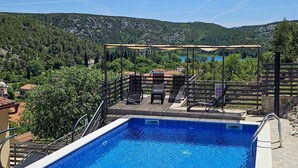 A swimming pool with a pergola and lounge chairs, surrounded by lush greenery and a mountainous backdrop. - 3 bedroom cozy home in Skradin (Skradin)