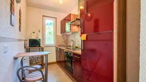 Cocina compacta con un refrigerador rojo, microondas, pileta y un pequeño comedor con una silla y mesa.
