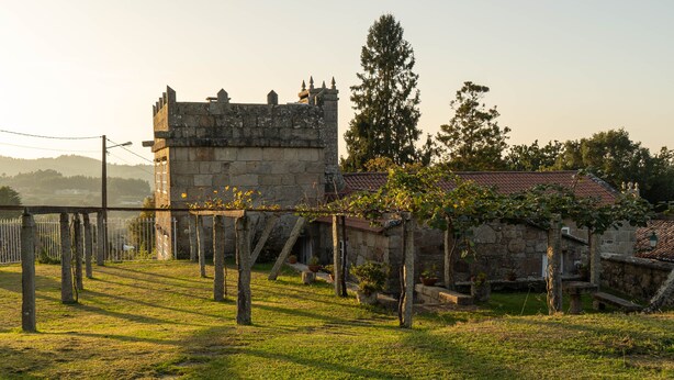 A stone building with a tower, surrounded by a fenced area with trees and a grassy lawn.