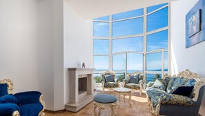Amplio salón con un gran ventanal que ofrece vistas panorámicas, muebles elegantes y una chimenea.