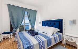 A bedroom with a large bed, a chair, a nightstand, and a view of the sea through a window. - Cozy home in Matulji with sauna (Matulji)