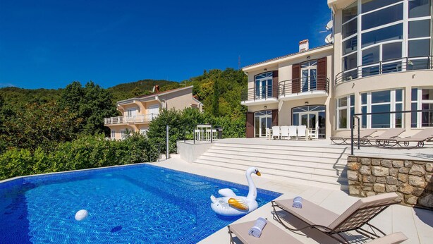 Una piscina con sillones de descanso y un flotador con forma de cisne, rodeada por un jardín ajardinado y un edificio de varios pisos con balcones.