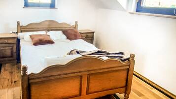 Ein Bett mit Holzbettgestell, einer weißen Bettdecke und zwei Kissen, ein Nachttisch und ein Fenster mit Jalousien.