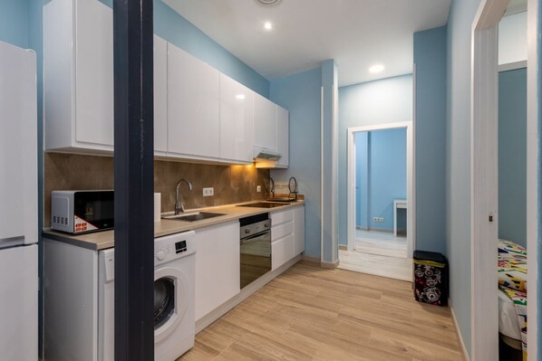 A compact kitchen with white cabinets, a microwave, a sink, and a washing machine.