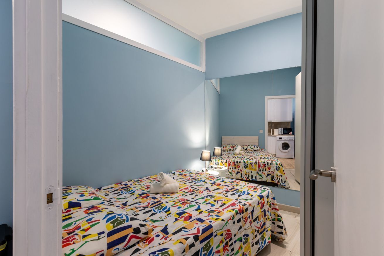 A bedroom with two beds, a washing machine, and a mirror reflecting the room.