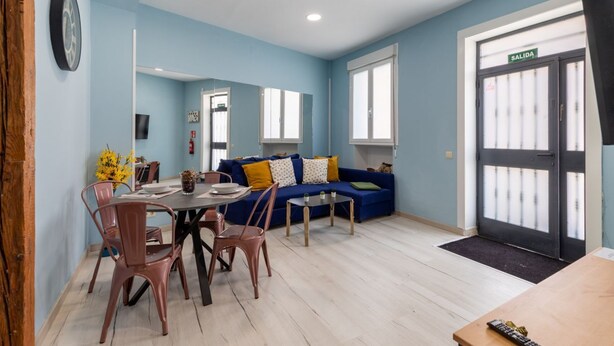 Ein Zimmer mit Esstisch, Stühlen, einer Couch, einem Fernseher und einer Tür mit der Aufschrift 'SALIDA'.