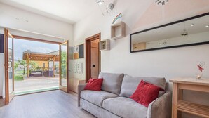 A modern living room with a grey sofa, red cushions, a wooden side table, and a glass candle holder.