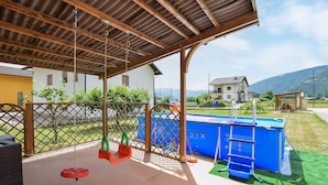 A covered patio with a pool, swings, and a view of houses and mountains.