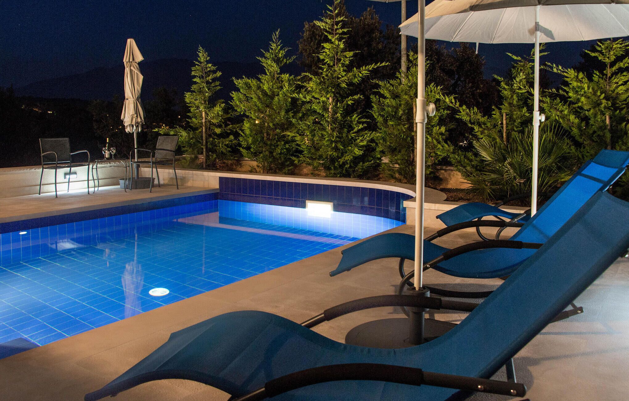 Una piscina con azulejos azules, sillas de descanso y una sombrilla.