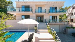 Uma casa moderna de dois andares com piscina, área de estar externa e escada que leva à entrada.