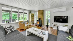 A modern living room with a fireplace, large windows, and a flat-screen TV. - 3 bedroom gorgeous home in Oksbøl (Oksbøl)
