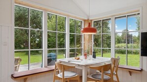A dining area with a white table and four wooden chairs, large windows offering a view of a green garden, and a red pendant light above the table. - Awesome home in Nykøbing Sj with WiFi (Nykøbing Sj)