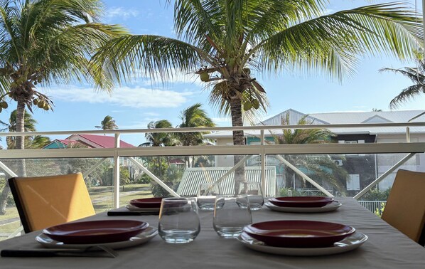 Mesa de comedor servida con platos y vasos, con vista a palmeras y casas.