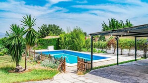 A swimming pool with a wooden fence, surrounded by lush greenery and a pergola.