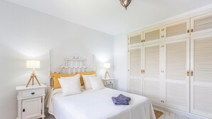 A bedroom with a bed, two bedside tables, a nightstand, a wardrobe, and a hanging light fixture.