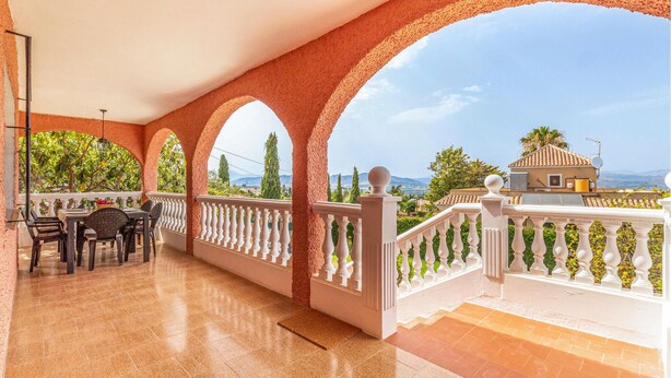 A covered outdoor area with a tiled floor, white balustrades, and a view of a distant building and landscape.