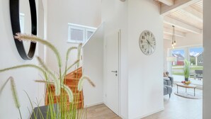 Un interior modern amb una escala de fusta, una porta blanca i vista a una zona residencial a través de grans finestres.