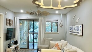 Un salón luminoso con una araña, televisor y comedor dispuesto con platos y una decoración de tiburón.