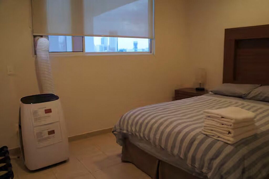 A hotel room with a bed, a nightstand, a lamp, and a window.